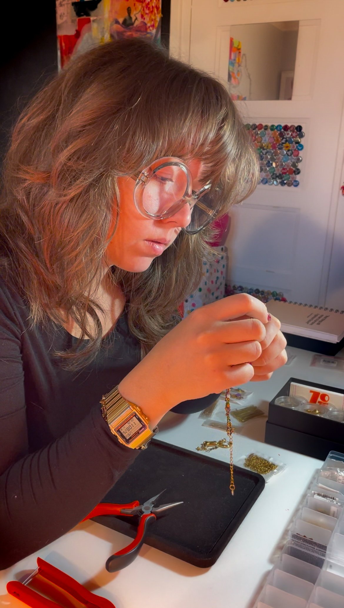 Moi dans mon atelier, lunettes rondes sur le nez, examinant entre mes doigts une chaîne fine